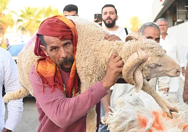 A man carries a sheep during Eid al-Adha at a market in Capital Governorate, Kuwait, June 16, 2024. (Photo by Asad/Xinhua)