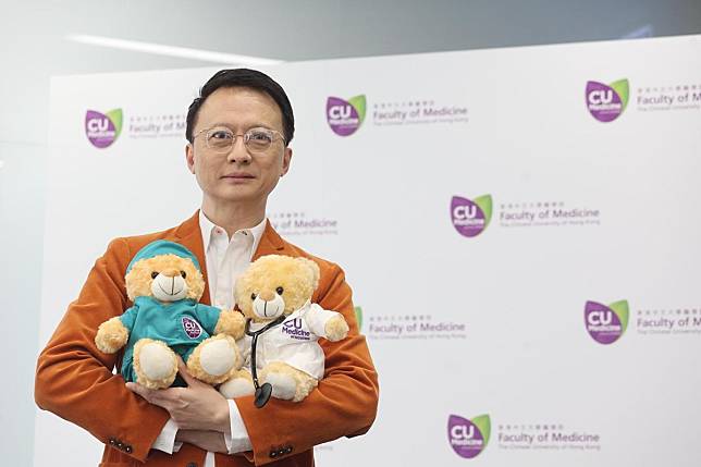 陳家亮今日身穿橘色西裝褸，抱着一對醫學院吉祥物熊仔見傳媒。