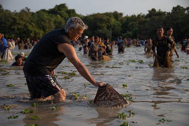 A foreign tourist tries to catch fish with a traditional woven bamboo trap during a traditional fish-catching ceremony in a lake in Siem Reap province, Cambodia on Feb. 9, 2025. (Photo by Sao Khuth/Xinhua)