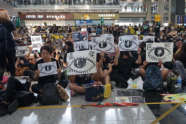 Protesters at Hong Kong International Airport on August 12 chant “police shot the girl, an eye for an eye” and hold up signs saying “give back the eye”, after a young woman was seriously injured during police firing of beanbag rounds in Tsim Sha Tsui the previous evening. Photo: Joanne Ma