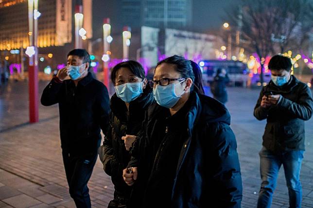 Pedestrians in Beijing wear protective masks to help stop the spread of a deadly virus that began in Wuhan. Photo: AFP