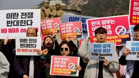 2026年3月16日，南韓首爾總統青瓦台外，抗議人士舉著標語牌，反對美國要求南韓向荷姆茲海峽派軍艦。路透社