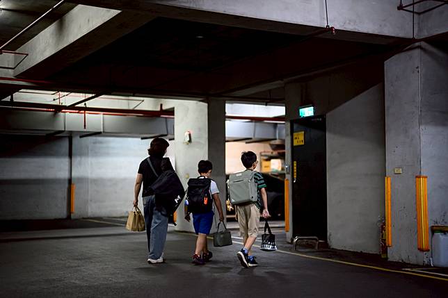 傍晚時分，家長帶著背負沉重書包的孩子穿過停車場。不少雙薪家庭對「有一孩聘外籍幫傭」新政策無感，是因為他們面臨的「時間貧窮」難題，最需要的並非24小時的「幫手」，而是支援接送、下班下課那2、3個小時的尖峰時刻，或有狀況時的臨時照顧需求。（攝影／黃世澤）