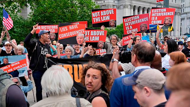 2024年5月30日，美國前總統川普在紐約曼哈頓刑事法院遭判34項罪名成立，有民眾在法院外舉牌。美聯社