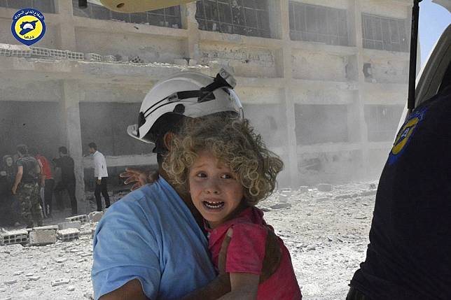 一名敘利亞「白盔隊」成員2017年救援一名遭空襲波及的孩童。（美聯社）