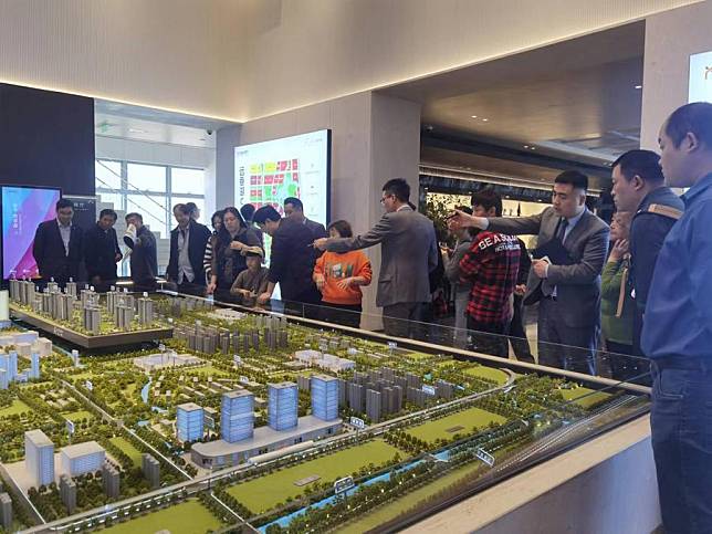 This photo taken with a mobile phone shows people watching a sand table model of a real estate project in east China's Shanghai, May 28, 2024. (Xinhua/Zheng Juntian)