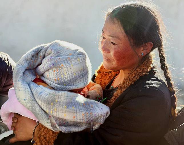 A woman holding her child receives warm clothes brought by volunteers in a village of Chamco Township, Dingri County, in Xigaze City, southwest China's Xizang Autonomous Region, Jan. 8, 2025. Rescue and relief efforts were made after a 6.8-magnitude earthquake struck Dingri County in southwest China's Xizang Autonomous Region on Jan. 7. (Xinhua/Jiang Fan)