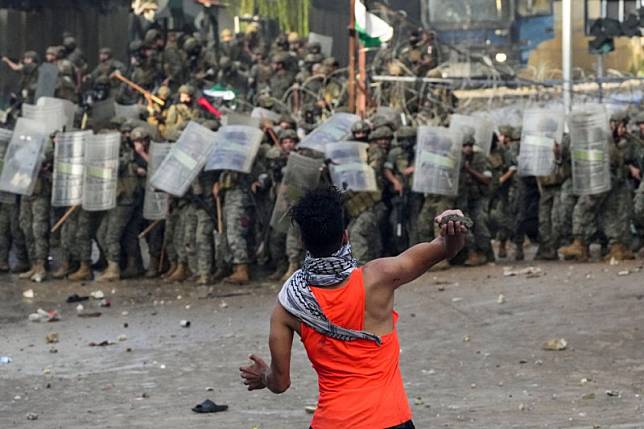 2023年10月18日，在黎巴嫩貝魯特北郊的美國大使館附近，一名抗議者在聲援加薩巴勒斯坦人的示威中朝警方丟擲石塊。（美聯社）