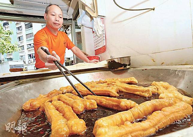 最佳位置——東哥隔着桌子俯身炸油條，看似不便，卻是其最佳位置，方便他一邊切、拉麵糰下鑊，一邊適時翻動鑊中的油條，讓油條炸得香脆透徹。（劉毓霖攝）