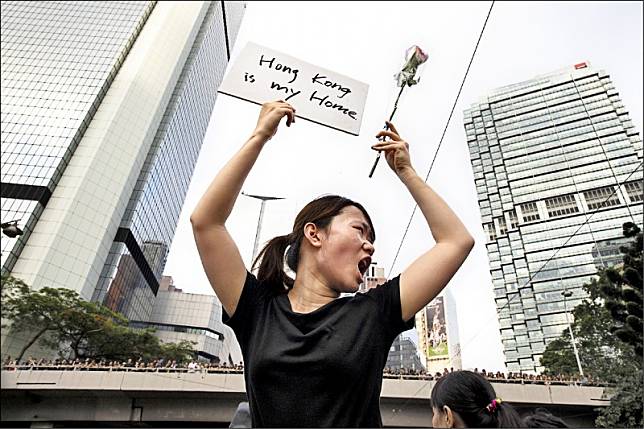香港「反送中」抗爭期間，一名女子手持鮮花及寫有「香港是我家」的標語。(彭博)