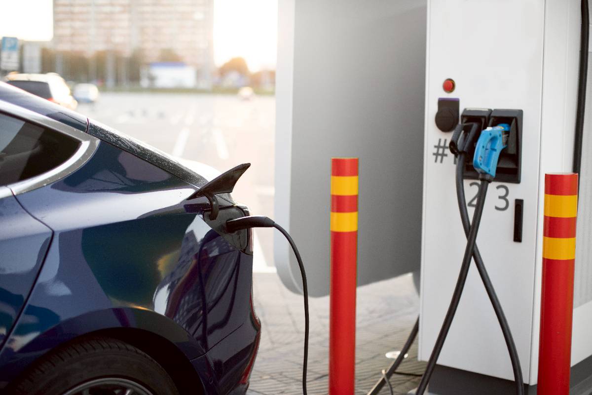 A blue electric vehicle is being charged at a public charging station, reflecting the UK's push for EV adoption, green policies, and impending tax reforms related to mileage-based fees and environmental regulations.