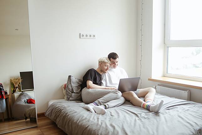 男性情侶開心地在床上一起看電腦。