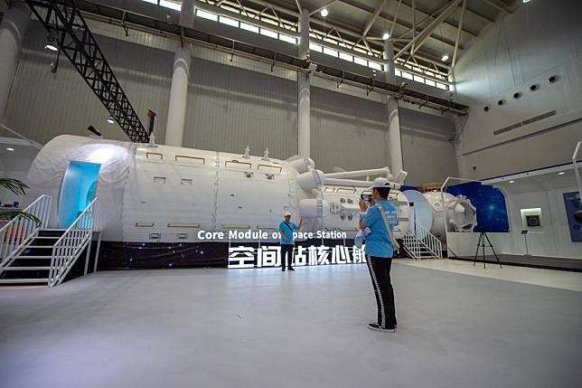 A visitor poses for a photo with a model of core module of space station at an exhibition on aerospace in Wuhan, central China's Hubei Province, April 23, 2024. (Xinhua/Hu Jingwen)