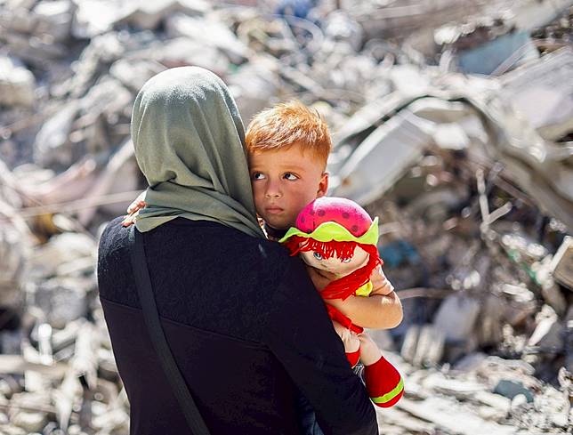 加薩走廊婦女馬麥爾（Inas Abu Maamar）1年前緊擁遭以軍空襲身亡侄女的屍體照片震驚全球。1年後，她帶著倖存的姪子重返姪女墓地，上方已覆蓋大量被炸毀的瓦礫石塊。路透社