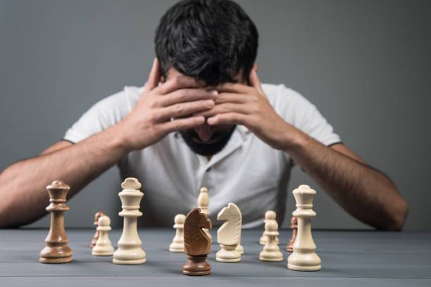 view of desperate man sitting in front of chess pieces on gray background