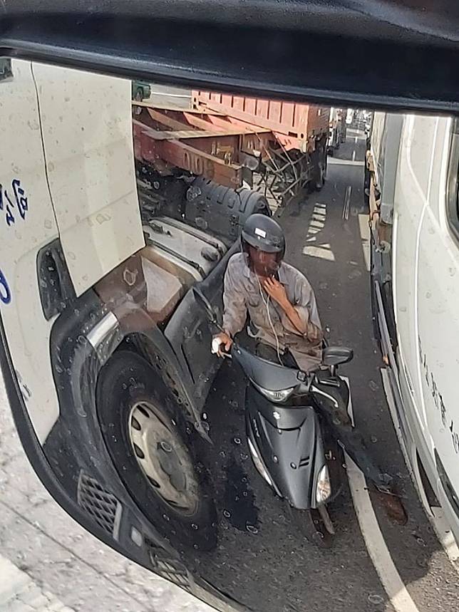 1名機車騎士躲在聯結車與大貨車之間閃避陽光，被網友痛批「不要命了」。(圖取自爆廢公社)